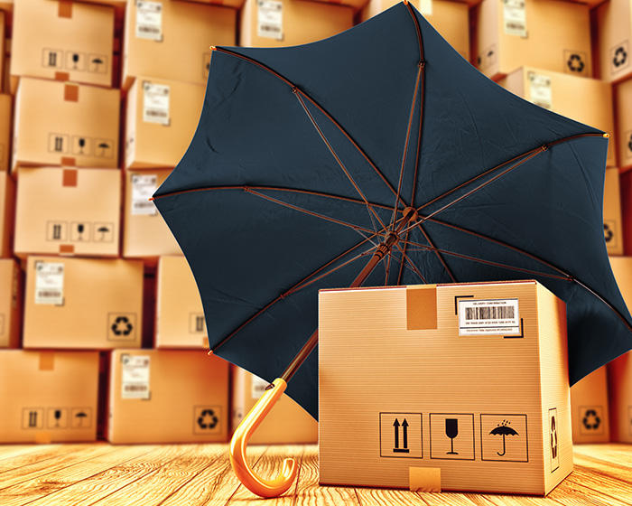 a box with an umbrella over it on a wooden floor with other shipping boxes piled up in the background